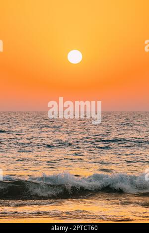 Sonnenuntergang Sonne Über Dem Meer. Natürlicher Sonnenaufgang Himmel Warme Farben Über Dem Meer. Meer Wasser Schaum Spritzer Waschen Sandstrand. Stockfoto