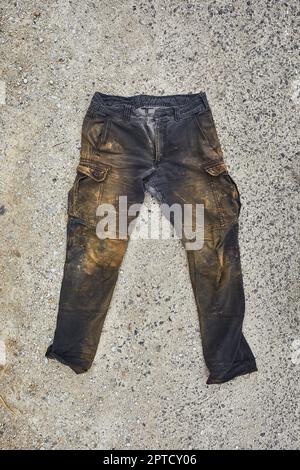 Zerrissene und dreckige Arbeitshose, mit Schlamm und Lehm bedeckt, auf dem Boden abgelegt Stockfoto