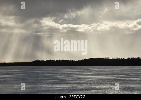 Am Horizont regnet es über dem gefrorenen See in Finnland Stockfoto