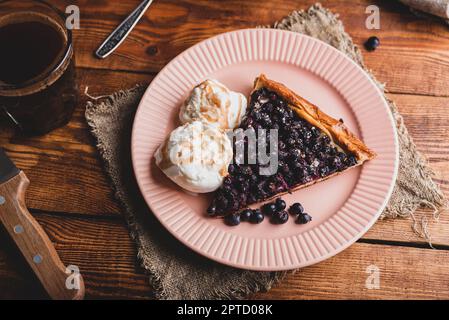 Eine Scheibe frisch gebackene Amelanchier Beeren Galette und zwei Schaufeln Vanille-Eis auf dem Teller über dem rustikalen Tisch Stockfoto