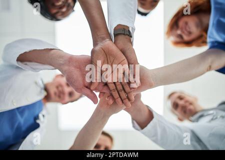 Zusammenarbeit, um den Qualitätsstandard der Gesundheitsversorgung aufrechtzuerhalten. Die Aufnahme aus dem unteren Winkel einer Gruppe von Praktizierenden, die ihre Hände in Unten zusammenfassen Stockfoto