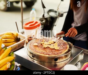 Bananen und Schokolade sind eine zeitlose Kombination. Ein unidentifizierbarer Lebensmittelhändler in Thailand, der einen leckeren Snack zubereitet Stockfoto