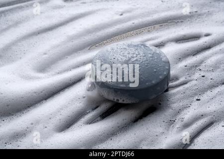 Schwarze, feste Seife, die vor einem Hintergrund aus Schaum platziert wird. Stockfoto