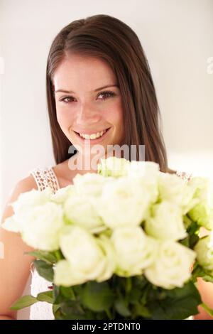 Sie ist so schön wie die Rosen, die sie in der Hand hält. Porträt einer schönen jungen Frau, die lächelt und einen Blumenstrauß in der Hand hält Stockfoto