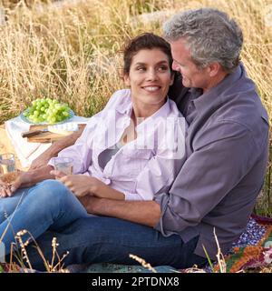 Nichts ist romantischer als ein Picknick. Ein liebevolles, reifes Paar, das zusammen ein intimes Picknick auf einem malerischen Feld genießt Stockfoto