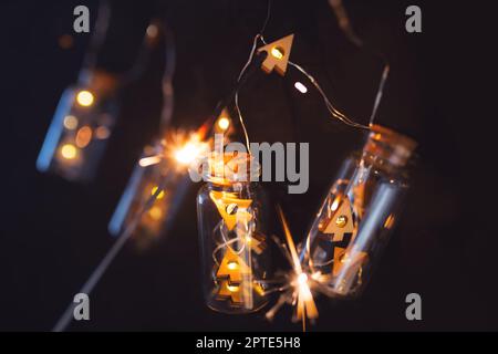 Weihnachtsglanz am dunklen Nachthimmel. Beleuchtete Leuchtkette in Glaszylindern mit glühendem Glitzer auf schwarzem Hintergrund. Weihnachten BA Stockfoto