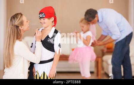 Die letzten Details hinzufügen. Ein lächelnder Junge, der vor seiner Mutter steht, der sich einen Schnurrbart im Gesicht malt, mit Vater und Schwester im Hintergrund Stockfoto