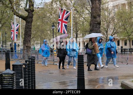 London, Großbritannien. An einem nassen Frühlingstag benutzen Touristen in der Mall Regenschirme und blaue Einwegponchos. Stockfoto