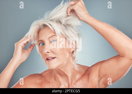 Seniorin, unschöne Haare und Stress für Friseurpflege, Kosmetik oder Schnitt vor grauem Studiohintergrund. Porträt einer älteren Frau mit schlechter Frisur Stockfoto