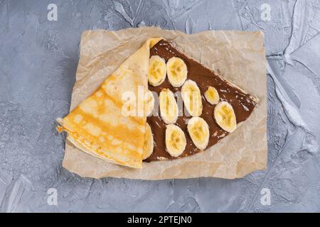Crepes gefüllt mit Schokolade und Banane auf weiße Platte. Dünne Pfannkuchen, Blini. Süße Nachspeise. Stockfoto
