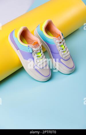 Nahaufnahme von trendigen farbigen Sneakers für Teenager-Mädchen auf buntem gelb-blauen Hintergrund. Weiße Sneakers mit Schnürsenkeln mit verschiedenen farbigen Einsätzen. S Stockfoto