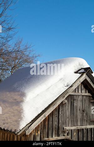 Schnee auf dem Dach eines Holzschuppens im Winter. Schönheit in der Natur an einem sonnigen Tag Stockfoto