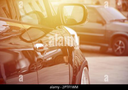 Diagonalansicht eines schwarz glänzenden Autos mit weißen Rädern, das auf einem Quadrat grauer Fliesen steht Stockfoto