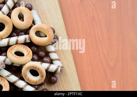 Knusprige Tuben, Schokoladenschmelzkugeln und Bagels liegen auf einer Holzfläche. Mischung aus verschiedenen Süßigkeiten Stockfoto