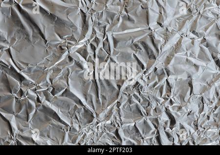 Dünnes, zerknittertes Blech aus zerkleinerter Aluminiumfolie mit glänzender, zerknitterter Oberfläche für Textur Stockfoto