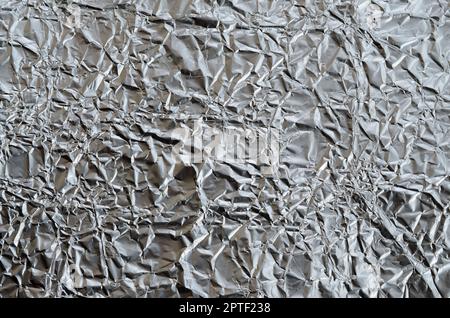 Dünnes, zerknittertes Blech aus zerkleinerter Aluminiumfolie mit glänzender, zerknitterter Oberfläche für Textur Stockfoto