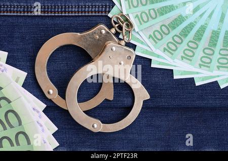 Der Fan von vielen Euro-Scheinen und Polizeihandschellen ist auf einer dunklen Jeansfläche. Hintergrundbild Stockfoto