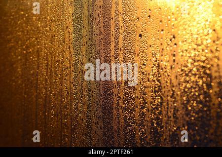 Die Textur von beschlagenem Glas mit vielen Tropfen und Kondensattropfen gegen das Sonnenlicht bei Sonnenaufgang. Hintergrundbild Stockfoto