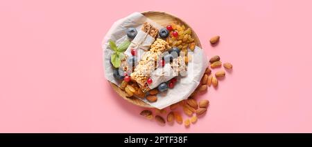 Teller mit gesunden Müsliriegeln, Beeren und Nüssen auf rosa Hintergrund Stockfoto