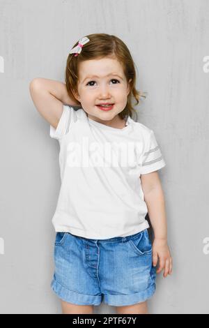 Zwei Jahre altes Mädchen in weißen T-Shorts und Jeans Shorts posiert im Studio Stockfoto