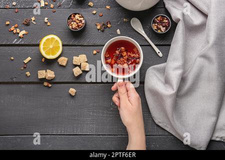 Komposition mit einer Frau, die eine Tasse heißen Obsttee auf einem schwarzen Holztisch hält Stockfoto