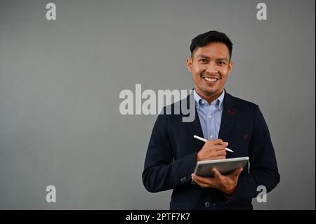 Das Porträt eines professionellen und erfolgreichen asiatischen Millennials im formellen Business-Anzug steht auf einem isolierten grauen Hintergrund mit seinem digitalen Hintergrund Stockfoto