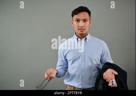 Unzufriedener und unglücklicher asiatischer Geschäftsmann, der auf einem isolierten grauen Hintergrund steht. Stockfoto