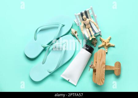 Komposition mit Strandaccessoires und hölzernen Schaufensterpuppen, die in einem kleinen Liegestuhl auf türkisfarbenem Hintergrund sitzen Stockfoto