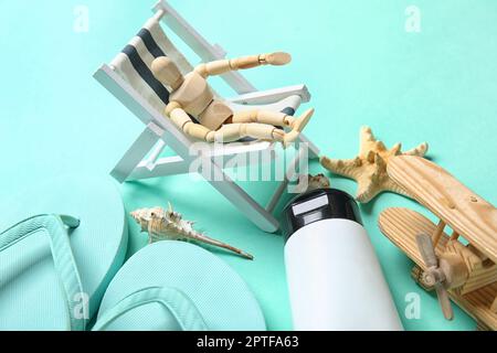 Komposition mit Strandaccessoires und hölzernen Schaufensterpuppen, die in einem kleinen Liegestuhl auf türkisfarbenem Hintergrund sitzen Stockfoto