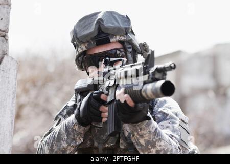 Kampfbereitschaft. Ein Soldat hockte sich neben eine kaputte Mauer und richtete seine Waffe in die Ferne Stockfoto