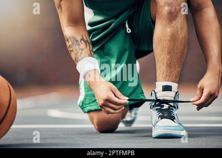 Basketballspielerschuhe auf dem Platz, Spiel starten und Hände binden Sneakers Schnürsenkel mit Ball. Sportmann bereiten sich auf den Wettbewerb, Spielertraining im Sommer Stockfoto