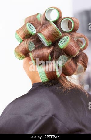 Schneiden wir. Rückansicht einer Frau mit Rollen im Haar beim Friseur Stockfoto