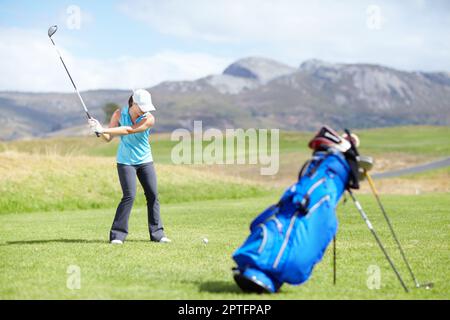 Ich schneide. Eine Golferin, die gerade einen Schuss mit einer verschwommenen Golftasche im Vordergrund macht Stockfoto