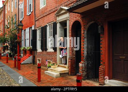 Eine junge Frau wartet darauf, dass ihr Kind zurückkommt, um seine Schultasche zu holen, die sie in der historischen Elfreth's Alley in Philadelphia vergessen haben Stockfoto