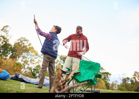 Bereiten wir das Lager vor. Ein Vater und ein Sohn, die zusammen ein Zelt aufstellen, während sie campen Stockfoto