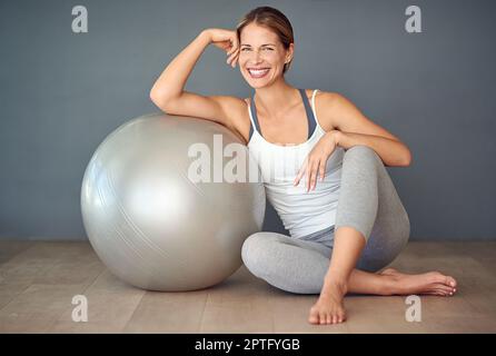 Spielen wir Ball. Eine sportliche junge Frau, die neben ihrem Fitnessball sitzt Stockfoto
