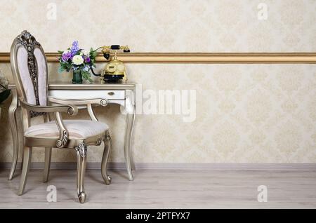 Ein Fragment eines retro Interieur mit einem Sessel und einen Schreibtisch, auf dem ein Telefon und eine Vase mit Blumen befindet. Stockfoto