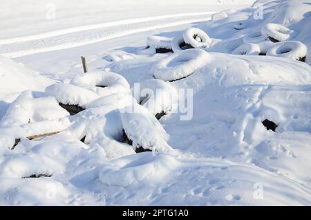 Gebrauchte und entsorgte Autoreifen liegen am Straßenrand und sind mit einer dicken Schneeschicht bedeckt Stockfoto