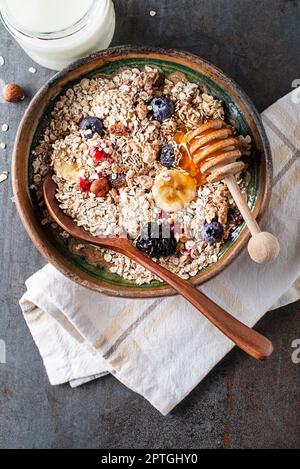 Eine Schüssel mit trockenem Müsli und Müsli serviert mit frischen Fruchtnüssen und Honig. Haferflockenplatte. Gesunde Ernährung, Ernährung. Draufsicht. Stockfoto