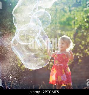 Das süße kleine Mädchen im Kleid spielt draußen mit riesigen Seifenblasen. Stockfoto