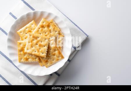 Viele Cracker auf einer Platte, die auf einem weißen Hintergrund mit Platz platziert ist. Blick von direkt oben. Stockfoto
