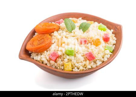 Bulgur-Brei mit getrockneten Aprikosen und kandierten Früchten in Tonschüssel isoliert auf weißem Hintergrund. Seitenansicht, Nahaufnahme. Traditionelle türkische Küche. Stockfoto