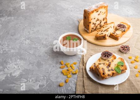 Hausgemachter Kuchen mit Rosinen, getrocknetem Kaki und einer Tasse heißer Schokolade auf grauem Betonboden und Leinentextilien. Seitenansicht, Kopierbereich. Stockfoto