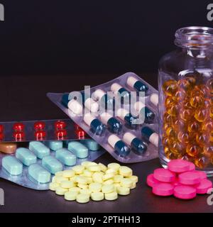 Pillen und Tabletten in verschiedenen Farben sind gestreut und in Flaschen auf dunklem Hintergrund Stockfoto