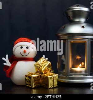 Weihnachtskomposition: Schneemann, Laterne mit Kerzen, leuchtend glänzende Boxen mit Geschenken, dunkelblauer Hintergrund, Platz für Logo, Schriftzug, Layout, Modell. Stockfoto