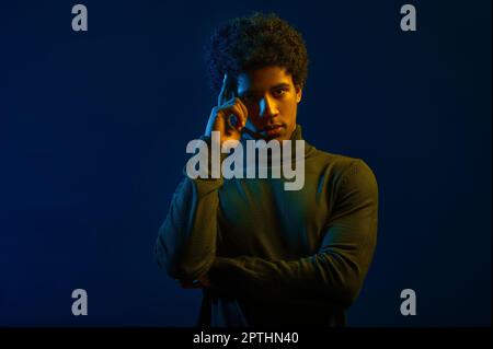 Porträt eines jungen Mannes, der den Finger am Tempel hält, vor dunklem Studiohintergrund Stockfoto