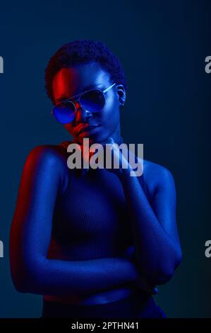 Nachdenkliche Frau in Sonnenbrille mit dunklem Studiohintergrund, Kopierbereich und Neonlicht Stockfoto