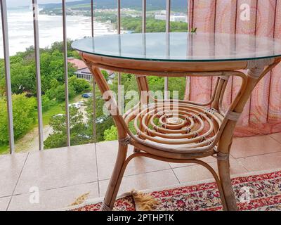 Innenraum des Balkons mit Korbtisch mit Glasdeckel, Blick vom Balkon auf die Küste. Stockfoto