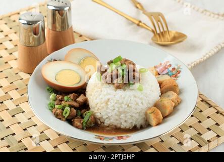 Nasi Bakmoy, gedämpfter Reis mit süßer und herzhafter Hühnersuppe mit Braunen gekochten Eiern und gehackten grünen Zwiebeln. Pearanakan Gericht, Indonesisches Menü Stockfoto