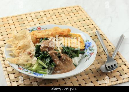 Nasi Pecel Madiun, gedämpfter Weißer Reis mit gekochtem Gemüse, Peyek, Tempeh, garniert mit würziger Erdnusssoße. Beliebtes Indonesisches Frühstücksmenü Stockfoto